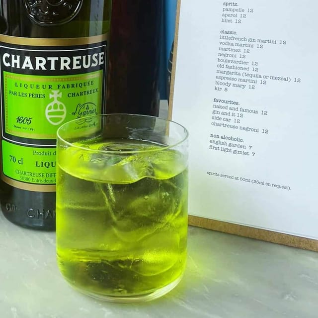 A glass of chartreuse beside their cocktail list