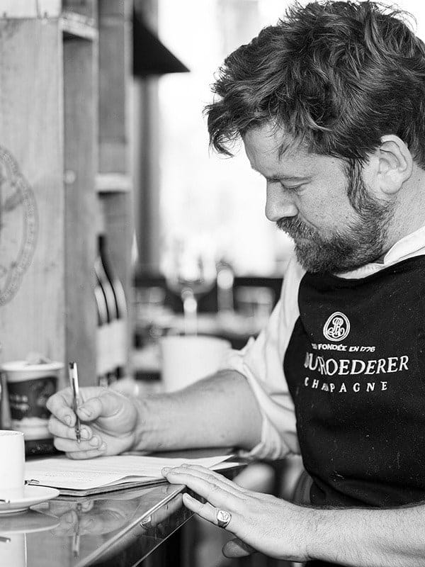 Freddy Bird writing the day's menu by hand, in black and white