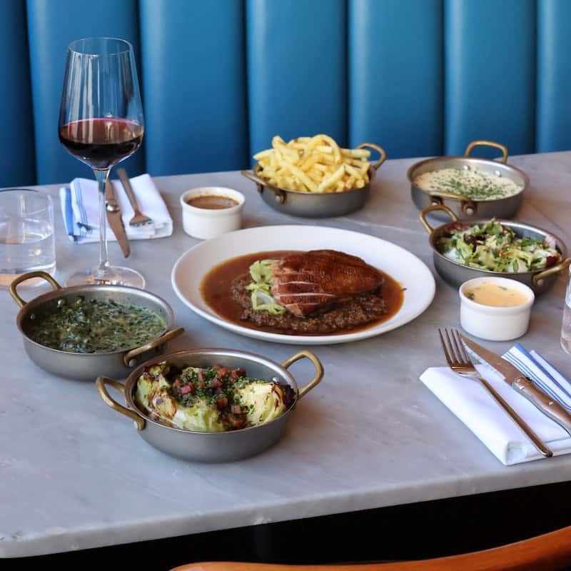 A main course with brass pans of sides, on the marble against the teal banquettes